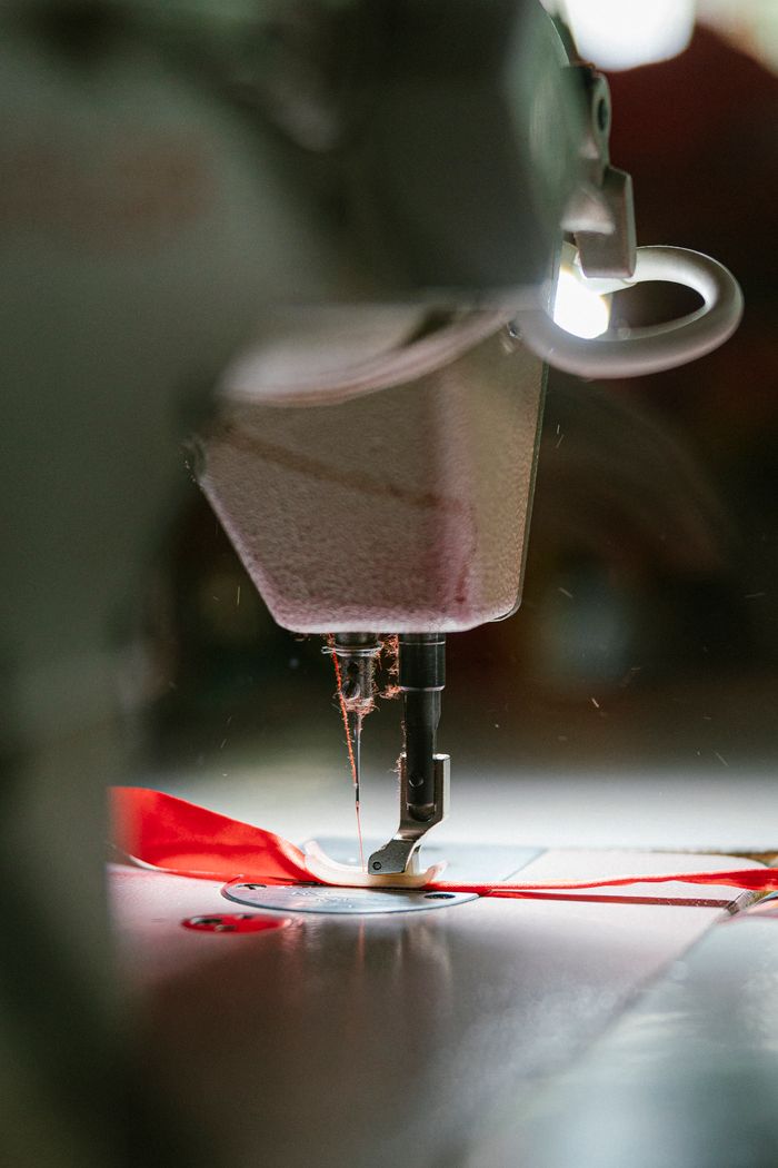 services-01 Detailed view of an industrial sewing machine working with red fabric, showing precision stitching.