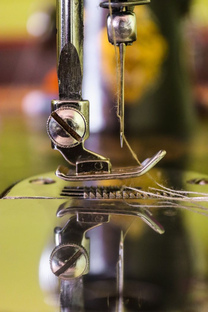 our-stories Detailed view of a sewing machine needle threading cloth, showcasing industrial precision.
