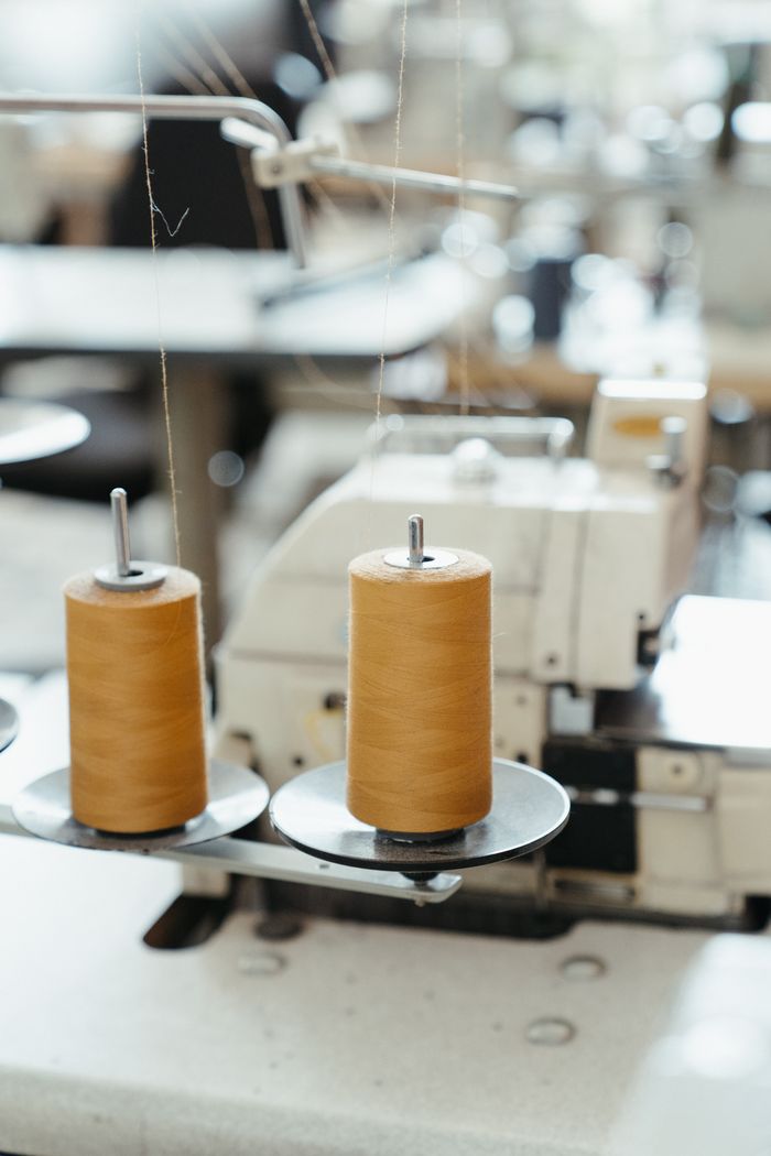 gallery-03 Detailed view of a sewing machine with spools of thread in a workshop setting.
