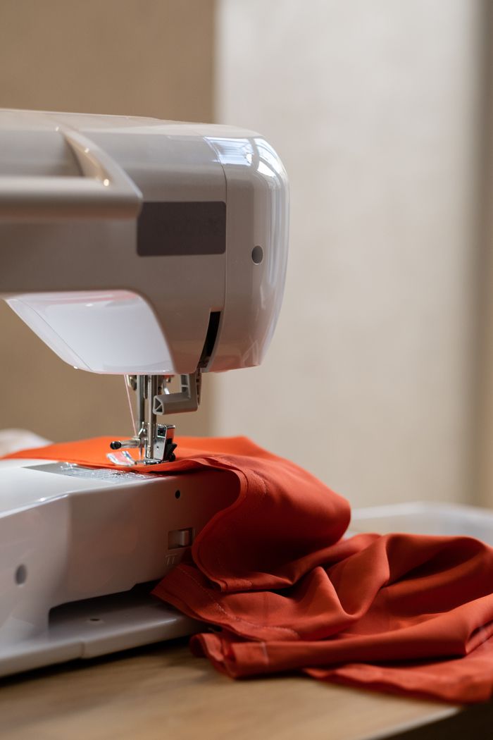 services-01 A sewing machine stitching orange fabric in a studio setting, showcasing fabric and craft.